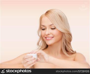 health, beauty and spa concept - smiling young woman opening cream over pink background