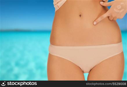 health, beauty and vacation concept - close up of woman pointing at her abs