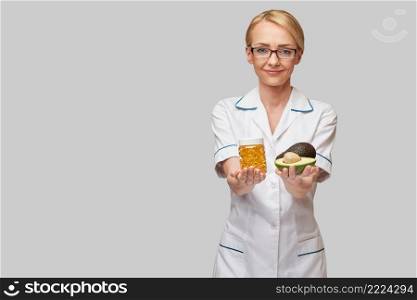 Health care and diet concept - doctor nutritionist or cardiologist holding fish oil in capsules for vitamin D and omega-3 fatty acids and avocado.. Health care and diet concept - doctor nutritionist or cardiologist holding fish oil in capsules for vitamin D and omega-3 fatty acids and avocado