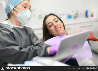 Health care concept - Female dentist showing tablet computer to woman patient at dental clinic office. High quality photo. Health care concept - Female dentist showing tablet computer to woman patient at dental clinic office.