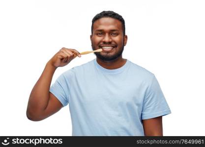 health care, dental hygiene and people concept - smiling african american young man with bamboo toothbrush cleaning teeth over white background. smiling african man with toothbrush cleaning teeth