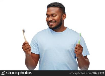 health care, dental hygiene and people concept - smiling african american young man with wooden and plastic toothbrushes over white background. african man with wooden and plastic toothbrushes