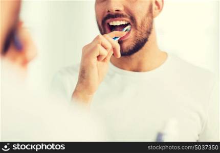 health care, dental hygiene, people and beauty concept - close up of young man with toothbrush cleaning teeth and looking to mirror at home bathroom. close up of man with toothbrush cleaning teeth