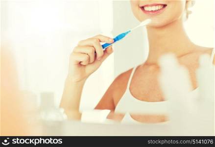 health care, dental hygiene, people and beauty concept - close up of smiling young woman with toothbrush cleaning teeth and looking to mirror at home bathroom. woman with toothbrush cleaning teeth at bathroom