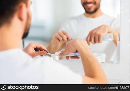 health care, dental hygiene, people and beauty concept - close up of young man cleaning teeth and squeezing toothpaste on toothbrush at home bathroom
