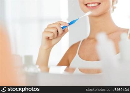 health care, dental hygiene, people and beauty concept - close up of smiling young woman with toothbrush cleaning teeth and looking to mirror at home bathroom