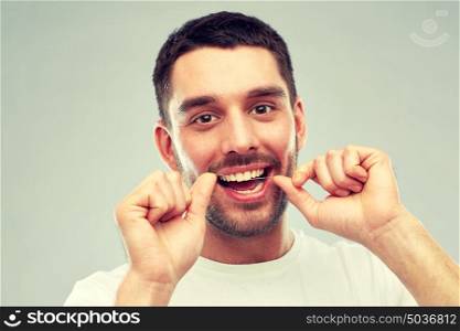 health care, dental hygiene, people and beauty concept - smiling young man with floss cleaning teeth over gray background. man with dental floss cleaning teeth over gray