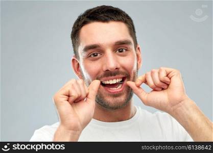 health care, dental hygiene, people and beauty concept - smiling young man with floss cleaning teeth over gray background