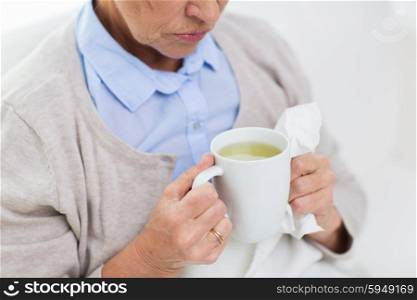 health care, flu, cold, age and people concept - close up of sick senior woman with paper napkin drinking hot tea at home