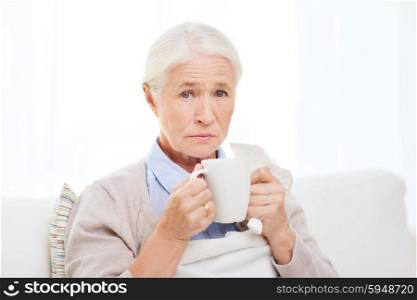 health care, flu, cold, age and people concept - sick senior woman with paper napkin drinking hot tea at home