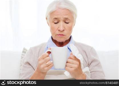 health care, flu, cold, age and people concept - sick senior woman with paper napkin drinking hot tea at home