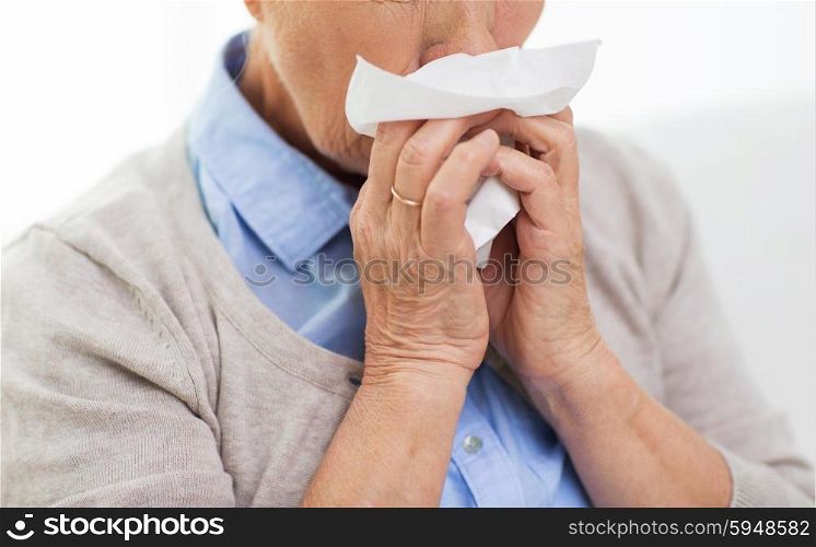 health care, flu, hygiene, age and people concept - close up of sick senior woman blowing nose to paper napkin at home