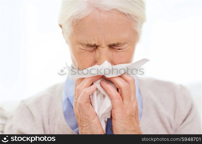 health care, flu, hygiene, age and people concept - sick senior woman blowing nose to paper napkin at home