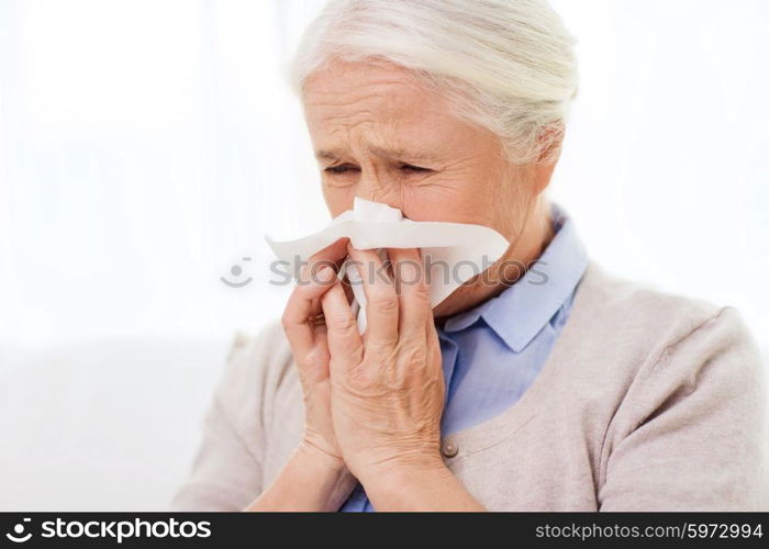 health care, flu, hygiene, age and people concept - sick senior woman blowing nose to paper napkin at home