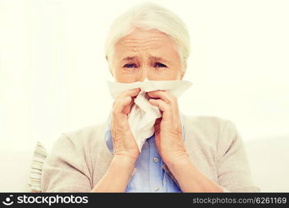 health care, flu, hygiene, age and people concept - sick senior woman blowing nose to paper napkin at home