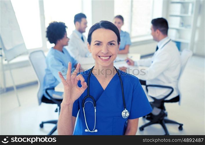 health care, gesture, profession, people and medicine concept - happy female doctor over group of medics meeting at hospital showing ok hand sign