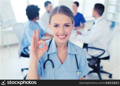 health care, gesture, profession, people and medicine concept - happy female doctor over group of medics meeting at hospital showing ok hand sign