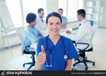 health care, gesture, profession, people and medicine concept - happy female doctor or nurse over group of medics meeting at hospital showing thumbs up gesture. happy doctor over group of medics at hospital
