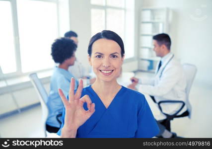 health care, gesture, profession, people and medicine concept - happy female doctor over group of medics meeting at hospital showing ok hand sign. happy doctor over group of medics at hospital