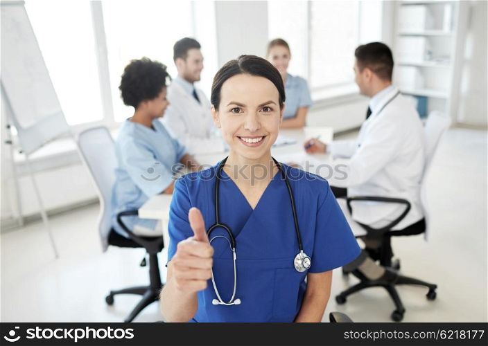 health care, gesture, profession, people and medicine concept - happy female doctor or nurse over group of medics meeting at hospital showing thumbs up gesture