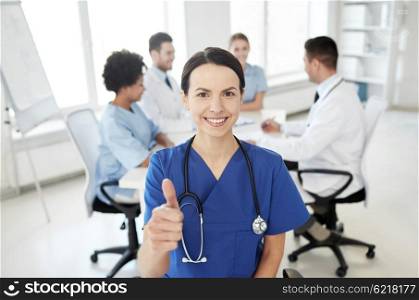 health care, gesture, profession, people and medicine concept - happy female doctor or nurse over group of medics meeting at hospital showing thumbs up gesture