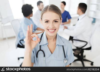 health care, gesture, profession, people and medicine concept - happy female doctor over group of medics meeting at hospital showing ok hand sign