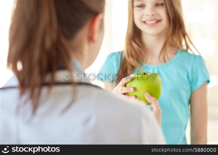 health care, healty eating, people, children and medicine concept - close up of doctor or stomatologist giving green apple to happy girl at hospital