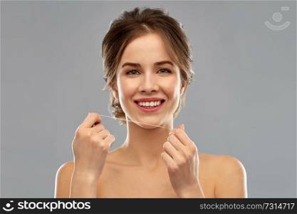 health care, hygiene and people concept - happy young woman with dental floss cleaning teeth over grey background. happy young woman with dental floss cleaning teeth