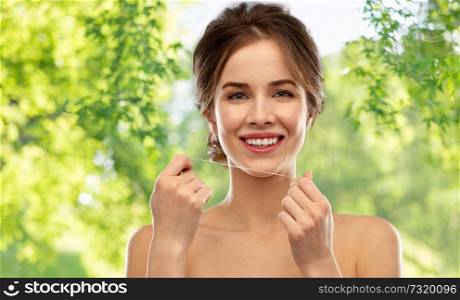 health care, hygiene and people concept - happy young woman with dental floss cleaning teeth over green natural background. happy young woman with dental floss cleaning teeth