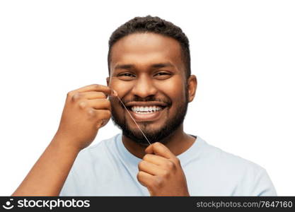 health care, hygiene and people concept - smiling african american young man with dental floss cleaning teeth over white background. happy african man with dental floss cleaning teeth