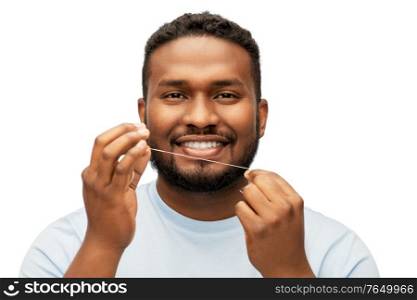 health care, hygiene and people concept - smiling african american young man with dental floss cleaning teeth over white background. happy african man with dental floss cleaning teeth