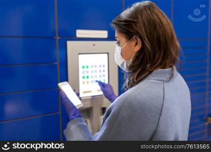 health care, mail delivery and pandemic concept - woman wearing face protective medical mask for protection from virus disease with smartphone entering code on automated parcel machine&rsquo;s touch screen. woman in mask with smartphone at parcel machine