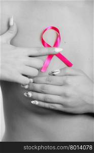 Health care medical concept. Closeup naked woman with pink breast cancer awareness ribbon, female checking her breasts for lumps. Black &amp;amp; white photo