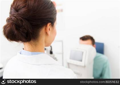 health care, medicine, people, eyesight and technology concept - close up of optometrist with autorefractor checking patient vision at eye clinic or optics store
