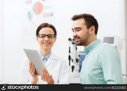 health care, medicine, people, eyesight and technology concept - female optician in glasses with tablet pc computer and man at eye clinic or optics store