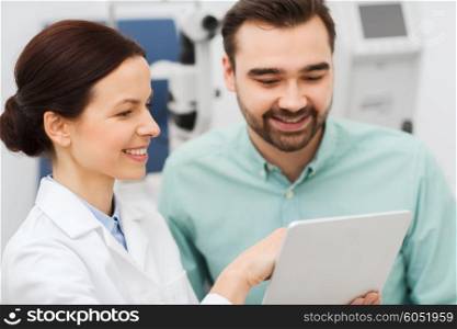 health care, medicine, people, eyesight and technology concept - female optician with tablet pc computer and man at eye clinic or optics store