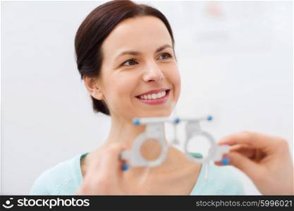 health care, medicine, people, eyesight and technology concept - happy woman having vision test with trial frame at eye clinic or optics store