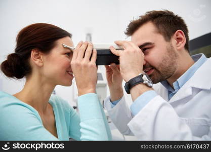 health care, medicine, people, eyesight and technology concept - optometrist with pupilometer checking patient intraocular pressure at eye clinic or optics store