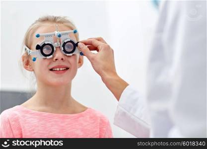 health care, medicine, people, eyesight and technology concept - optometrist with trial frame checking girl patient vision at eye clinic or optics store