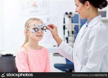 health care, medicine, people, eyesight and technology concept - optometrist with trial frame checking girl patient vision at eye clinic or optics store