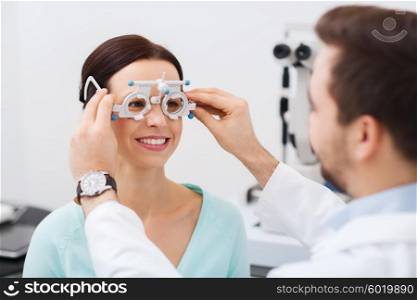 health care, medicine, people, eyesight and technology concept - optometrist with trial frame checking patient vision at eye clinic or optics store