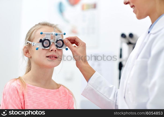 health care, medicine, people, eyesight and technology concept - optometrist with trial frame checking girl patient vision at eye clinic or optics store