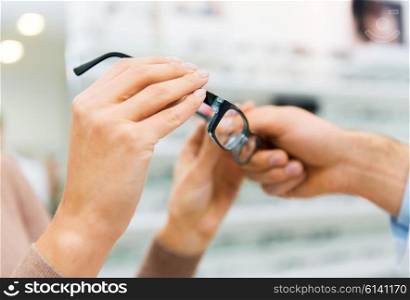 health care, people, eyesight and vision concept - close up of hands with glasses at optics store