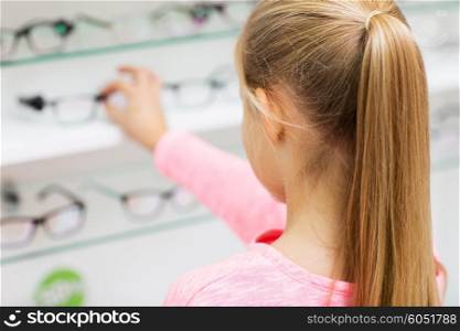 health care, people, eyesight and vision concept - close up of little girl choosing glasses at optics store