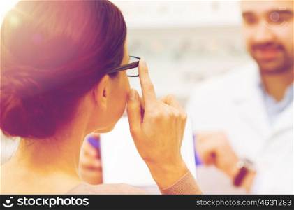 health care, people, eyesight and vision concept - close up of optician and woman choosing glasses at optics store
