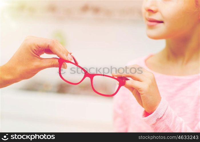 health care, people, eyesight and vision concept - close up of optician giving glasses to little girl at optics store