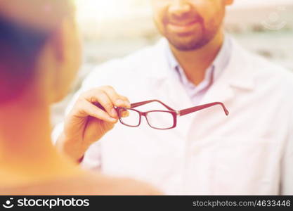 health care, people, eyesight and vision concept - close up of optician showing glasses to woman at optics store