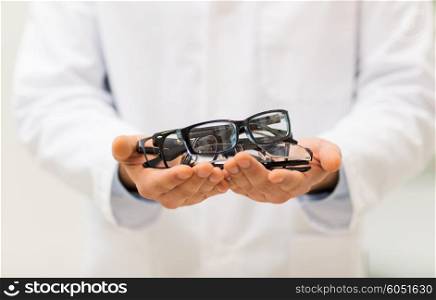 health care, people, eyesight and vision concept - close up of optician hands holding glasses at optics store