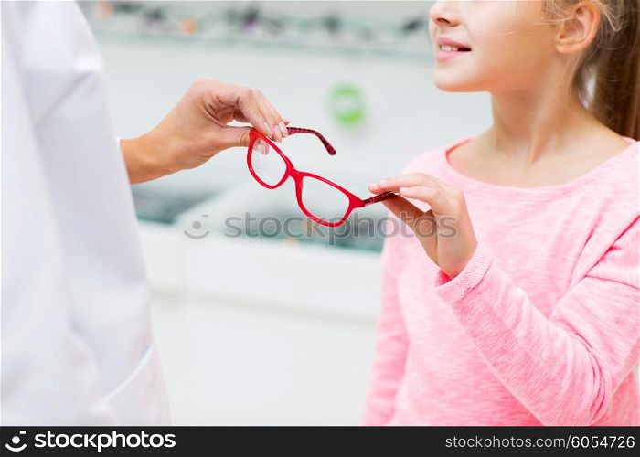 health care, people, eyesight and vision concept - close up of optician giving glasses to little girl at optics store