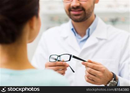 health care, people, eyesight and vision concept - close up of optician showing glasses to woman at optics store